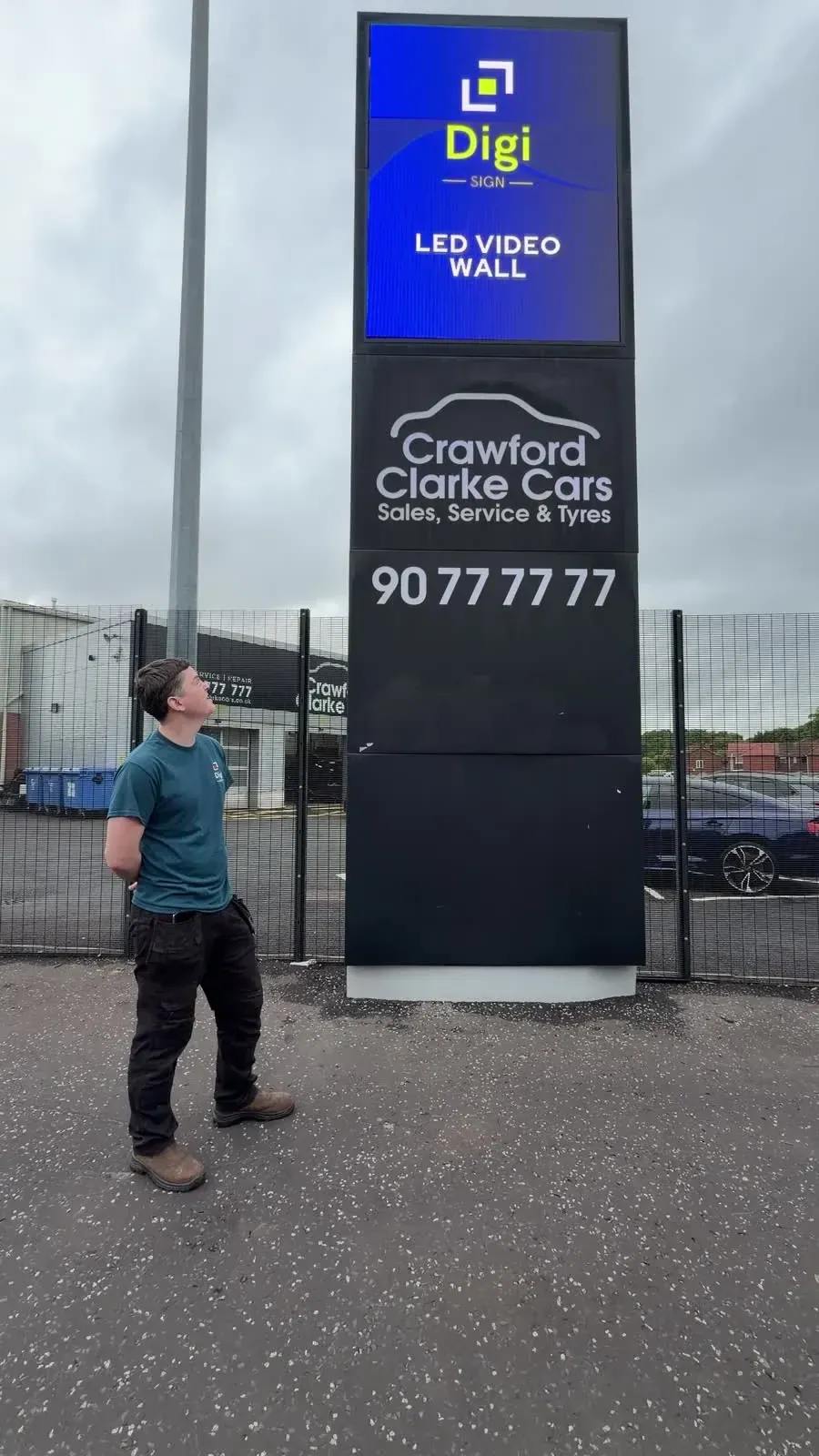 Full-height view of the working Crawford Clarke LED totem with an installer at ground level